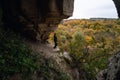 Woman standing by lighted exit in cave, daytime. Atmospheric snapshot in natural rock formations with autumn forest and dramatic