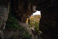 Woman standing by lighted exit in cave, daytime. Atmospheric snapshot in natural rock formations with autumn forest and dramatic