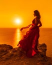 A woman is standing in a long red dress, a fashion model in an evening dress, soaring over the sea Royalty Free Stock Photo