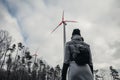 Woman standing and looking on  wind turbine station near forest  in bad weather conditions - environmental problem concept Royalty Free Stock Photo