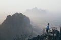 Woman standing on mountain peak with stairs going down during sunrise foggy morning in Hpa-An, Myanmar