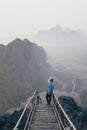 Woman standing on mountain peak with stairs going down during sunrise foggy morning in Hpa-An, Myanmar