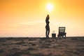 Woman standing near sun lounger and taking off her clother. Beach at sunset