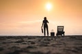 Woman standing near sun lounger and taking off her clother. Beach at sunset