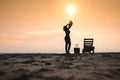 Woman standing near sun lounger and taking off her clother. Beach at sunset