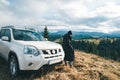 Woman standing near suv car at hill peak looking at beautiful view of mountains Royalty Free Stock Photo