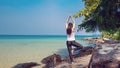 A woman standing on one leg while practicing yoga on wooden bridge over the sea during summer vacation. Royalty Free Stock Photo