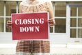 Woman Standing Outside Empty Shop Holding Closing Down Sign