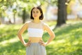 A woman is standing in a park, wearing a white tank top and grey sweatpants Royalty Free Stock Photo