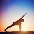 Woman standing in revolved side angle yoga pose meditating at sunset