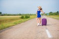 A woman is standing on the road with a hat and with a big bag. Girl in a blue tight-fitting dress with a purple suitcase Royalty Free Stock Photo