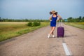 A woman is standing on the road with a hat and with a big bag. Girl in a blue tight-fitting dress with a purple suitcase Royalty Free Stock Photo