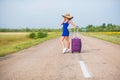 A woman is standing on the road with a hat and with a big bag. Girl in a blue tight-fitting dress with a purple suitcase Royalty Free Stock Photo