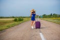 A woman is standing on the road with a hat and with a big bag. Girl in a blue tight-fitting dress with a purple suitcase Royalty Free Stock Photo