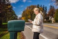 Woman standing beside a roadside mailbox on a bright autumn day, holding a stack of letters while checking her mail Royalty Free Stock Photo