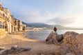 Woman standing on a rock looking at the view of houses and long sandy beach in the old harbour on a sunny day in Cefalu, Sicily, Royalty Free Stock Photo