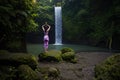 Woman standing on the rock, practicing yoga. Young woman raising arms with namaste mudra near waterfall. Healthy life concept.