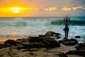 Woman standing on the rock, practicing yoga. Young woman raising arms witih namaste mudra at the beach. Bali