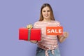 Woman standing with sale card and red present box in hands, discounts for holidays. Royalty Free Stock Photo