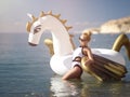 Woman standing on sea shore beach near resort hotel with giant inflatable unicorn pegasus float mattress in white bikini Royalty Free Stock Photo