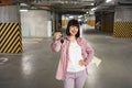 Woman standing in underground parking lot in casual clothes holding keys.