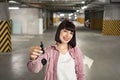 Woman standing in underground parking lot in casual clothes holding keys.