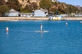 A woman standing up on paddle board rowing across the vast deep blue ocean water in the Dana Point Harbor surrounded by buoys