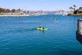 A woman standing up on paddle board rowing across the vast deep blue ocean water in the Dana Point Harbor surrounded by buoys