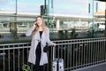 Woman standing with valise and talking by smartpone near airport. Royalty Free Stock Photo