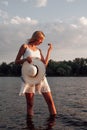 A woman is standing in the water. A beautiful young blonde in a white summer dress and a white straw hat with a black Royalty Free Stock Photo