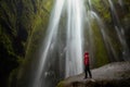 Woamn wearing a red jacket at the foot of beautiful waterfall in a canyon