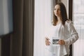 Pregnant woman stands by the window and looks at photo