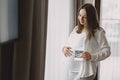 Pregnant woman stands by the window and looks at photo