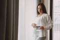 Pregnant woman stands by the window and looks at photo