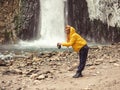A woman stands against the backdrop of a stormy waterfall flowing down from wet, icy rocks, filling her hat with water