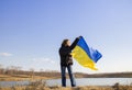 woman stands against the background of the lake and holds the Ukrainian yellow-blue flag against the sky Royalty Free Stock Photo