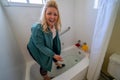 Woman stands in a bathtub and washes her feet and her shoes, with a big smile and happy look on her face