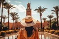 A woman stands in front of a fountain, wearing a hat, View from askance A woman holding a bunch of vibrant love heart balloons,