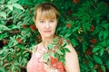 Woman stands in green bushes with red berries. Portrait of a woman of Slavic appearance