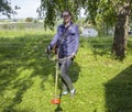 A woman stands with a hand trimmer for mowing grass