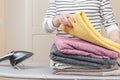 Woman stands by an ironing board with an iron and is folding a stack of ironed, clean terry towels