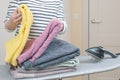 Woman stands by an ironing board with an iron and is folding a stack of ironed, clean terry towels