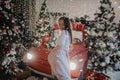 Woman stands near Christmas tree and retro car against background of snowfall Royalty Free Stock Photo