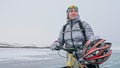 Woman stands near her bike on ice. The girl cyclist stopped to r Royalty Free Stock Photo