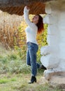 A woman stands near the old house with thatched roof. Hands raised up and smiling Royalty Free Stock Photo