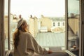 A woman stands near the window against the backdrop of the roofs of Paris. A girl with long hair in a beige suit and a beret