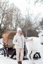 a woman stands next to a white horse in nature.