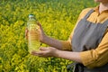 A woman stands in a rape field and holds a bottle of rapeseed oil in his hands.