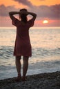 Woman stands on seacoast on sunset, rear view