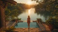a woman is standing next to a swimming pool overlooking a lake at sunset Royalty Free Stock Photo